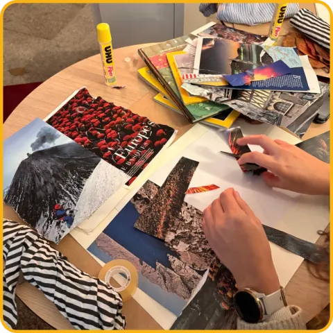 Mãos a recortar e colar imagens de revistas numa mesa cheia de papéis.