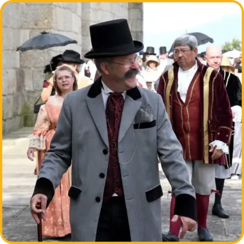 Homens vestidos à época de Camilo Castelo Branco, de cartola e sobrecasaca, num cortejo histórico numa rua de pedra.