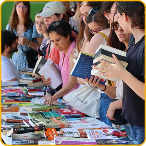 Muitas pessoas a escolher livros espalhados numa mesa.